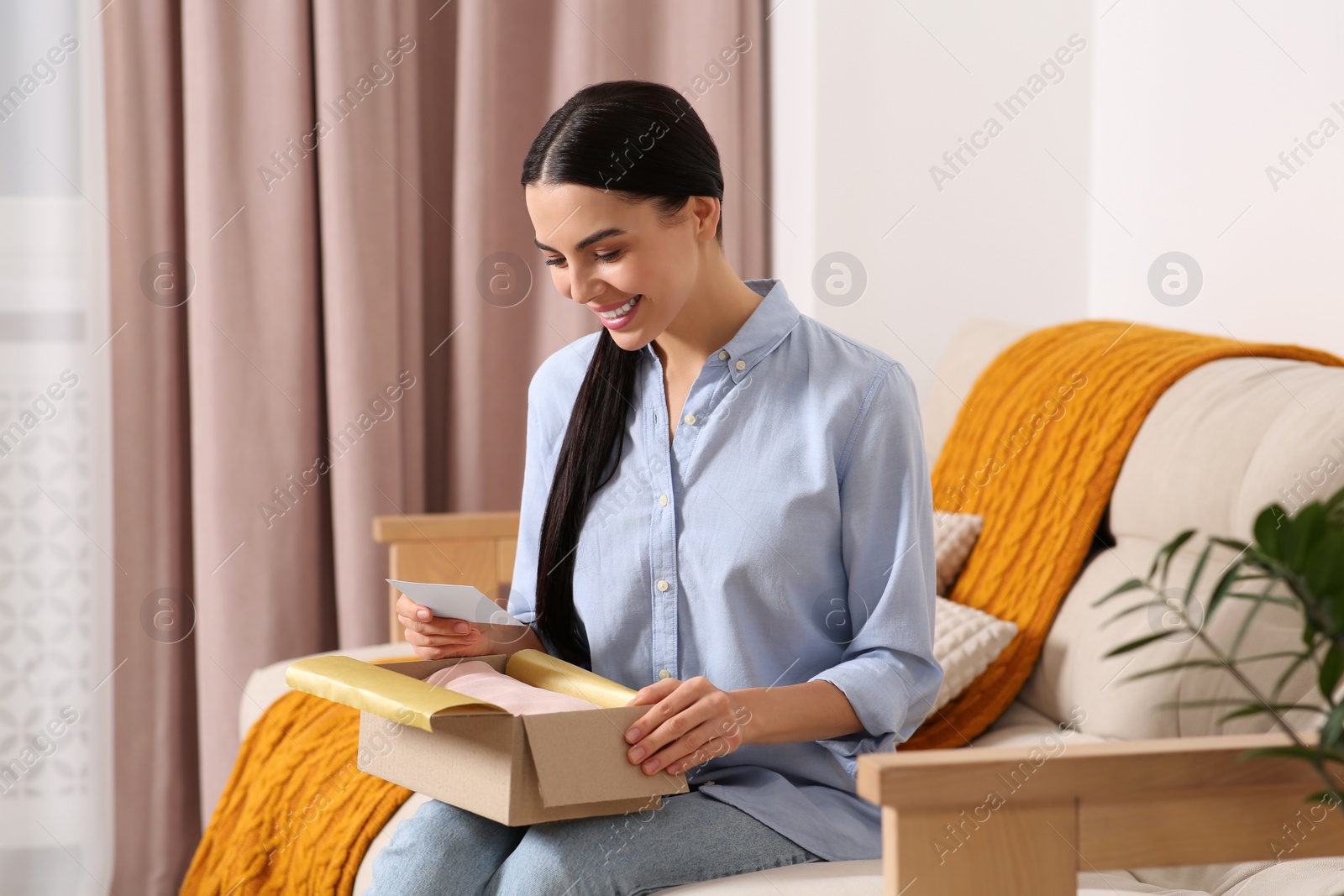 Photo of Happy woman holding greeting card and parcel with Christmas gift at home