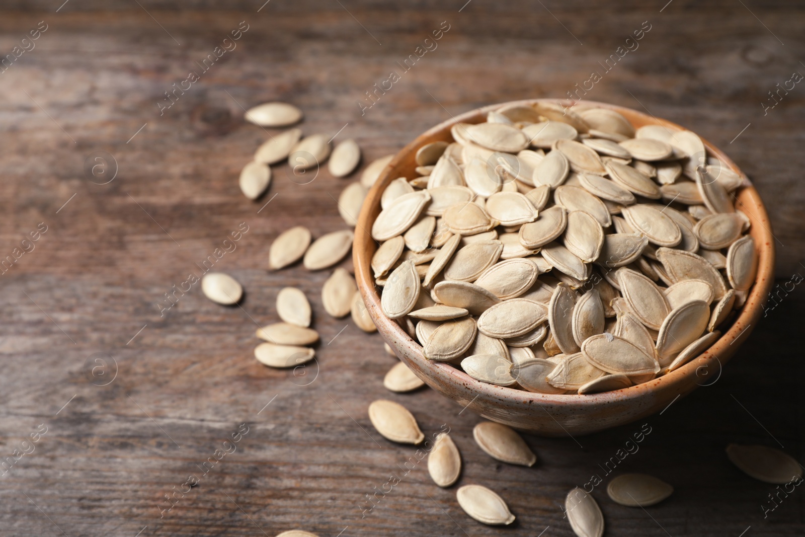 Photo of Full bowl of raw pumpkin seeds on wooden background