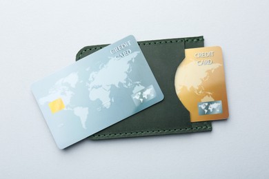 Photo of Woman holding leather card holder with credit cards on light grey background, top view