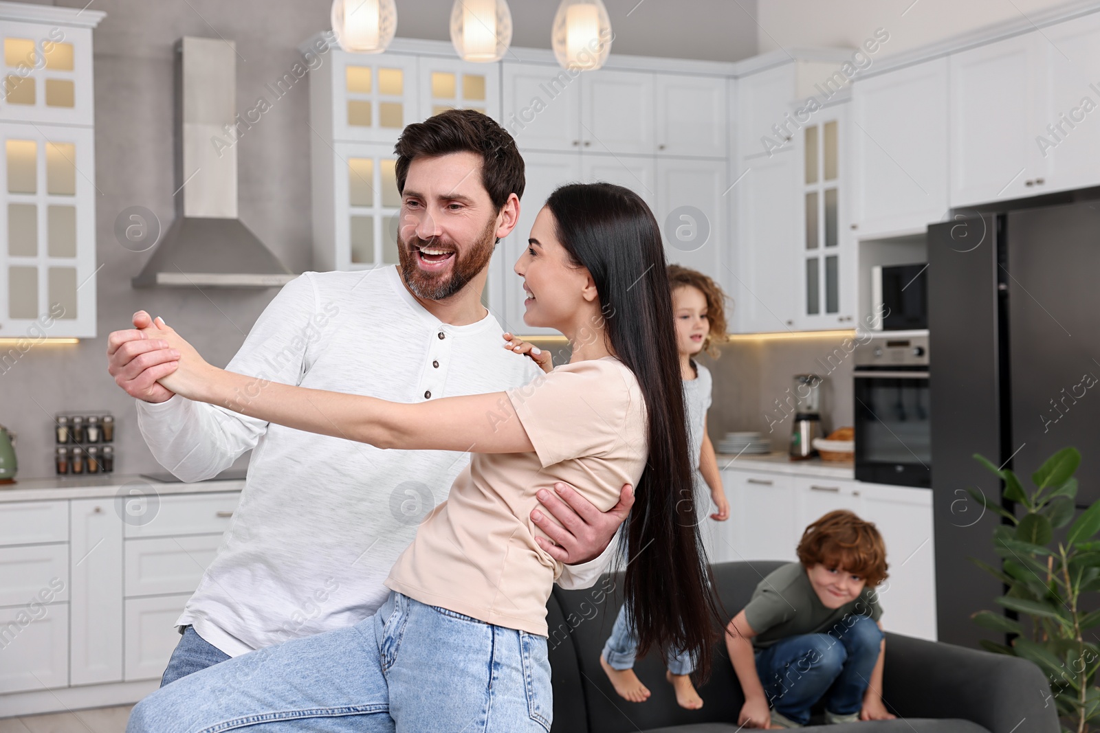 Photo of Happy family having fun at home. Couple dancing while children jumping on sofa