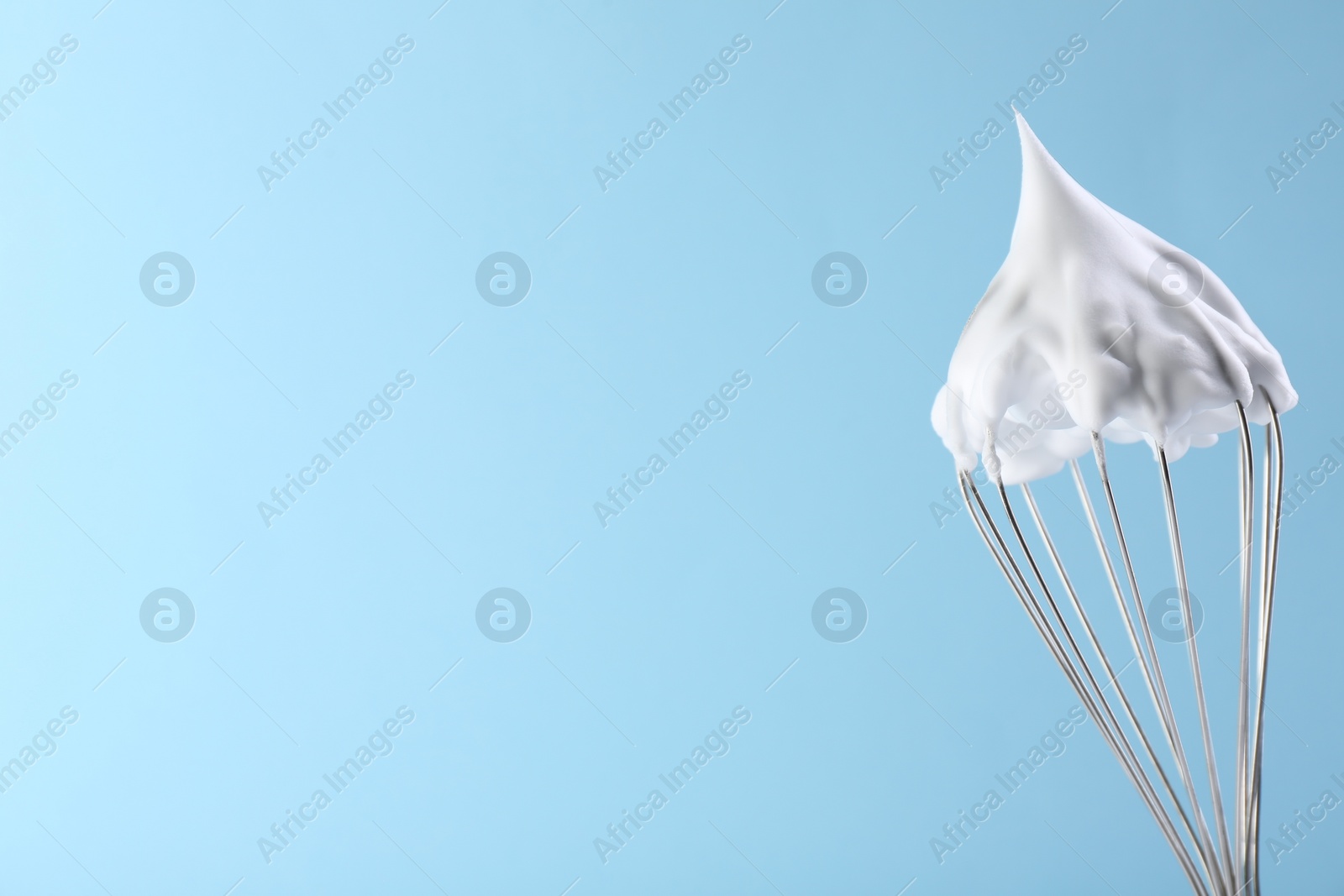 Photo of Whisk with whipped cream on light blue background. Space for text