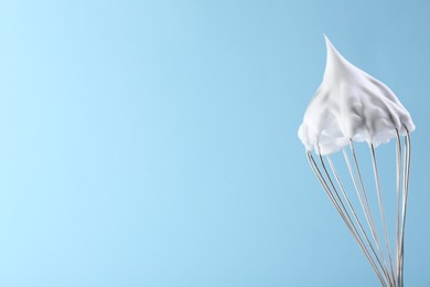 Photo of Whisk with whipped cream on light blue background. Space for text