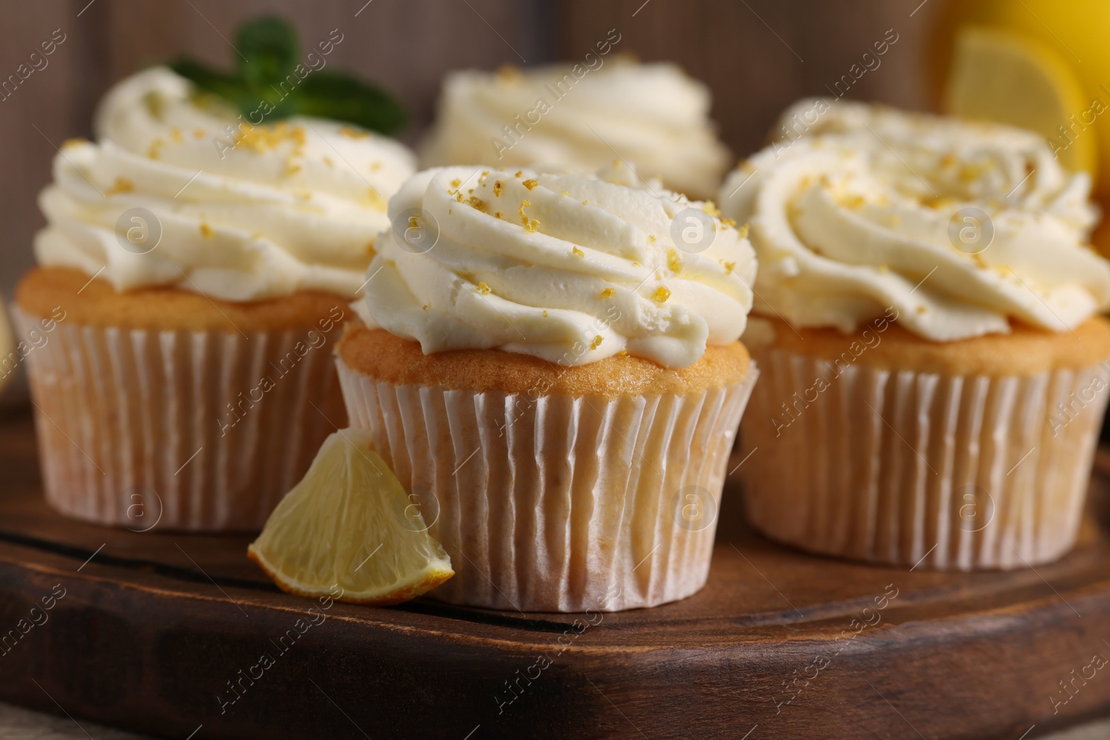 Photo of Delicious cupcakes with white cream and lemon zest on wooden board, closeup