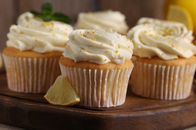 Delicious cupcakes with white cream and lemon zest on wooden board, closeup