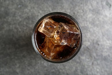 Glass of refreshing soda water with ice cubes on grey table, top view