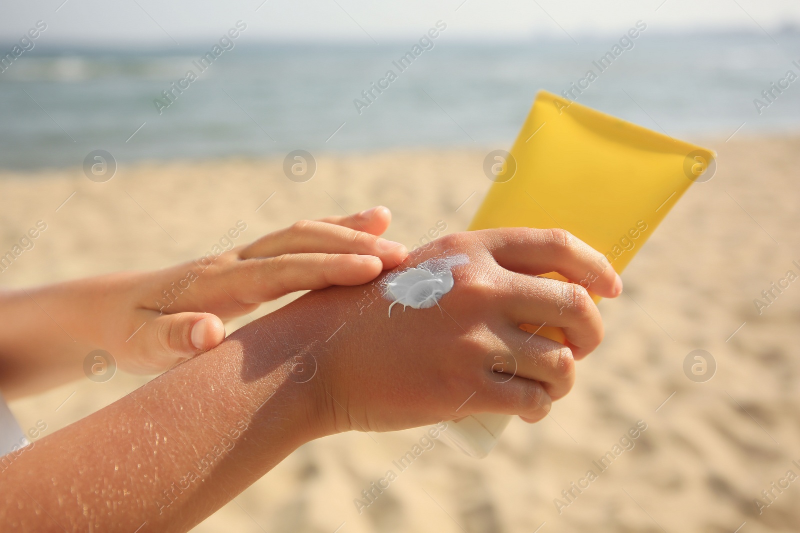 Photo of Child applying sunscreen near sea, closeup. Sun protection care