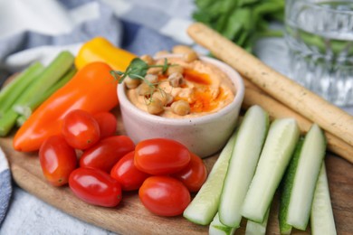 Board with delicious hummus, grissini sticks and fresh vegetables, closeup