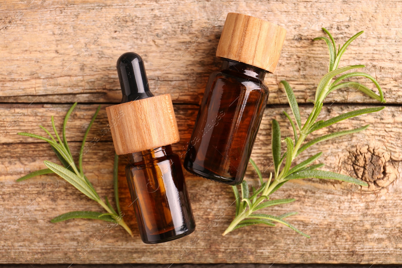 Photo of Aromatic essential oils in bottles and rosemary on wooden table, flat lay