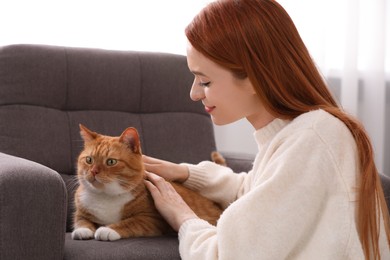 Woman stroking her cute cat in armchair at home