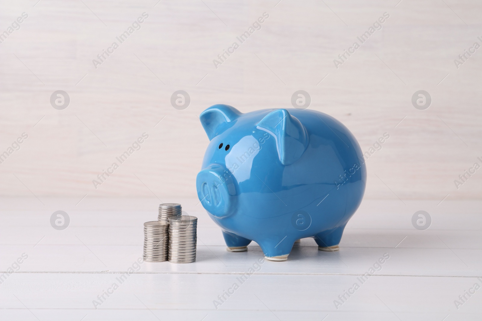 Photo of Financial savings. Piggy bank and stacked coins on white wooden table