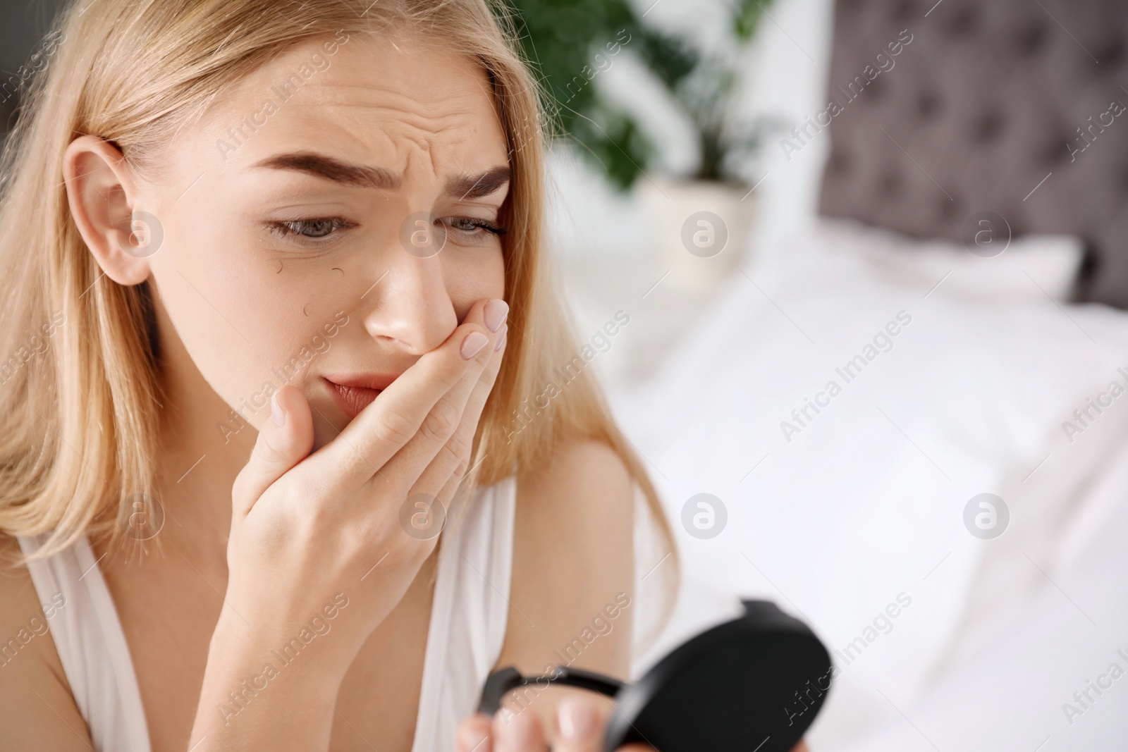 Photo of Young woman with eyelash loss problem looking in mirror indoors