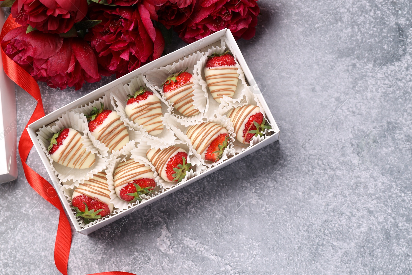 Photo of Delicious chocolate covered strawberries in box and flowers on light grey table, flat lay. Space for text