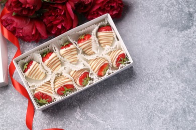 Delicious chocolate covered strawberries in box and flowers on light grey table, flat lay. Space for text