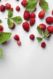 Many fresh wild strawberries and leaves on white background, flat lay. Space for text