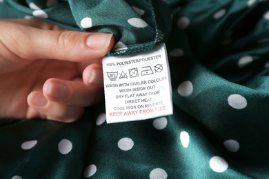Photo of Woman reading clothing label with care instructions and content information on green polka dot garment, closeup