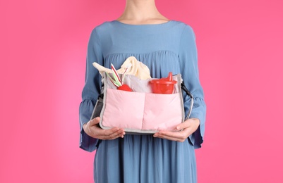 Photo of Woman holding maternity bag with baby accessories on color background, closeup