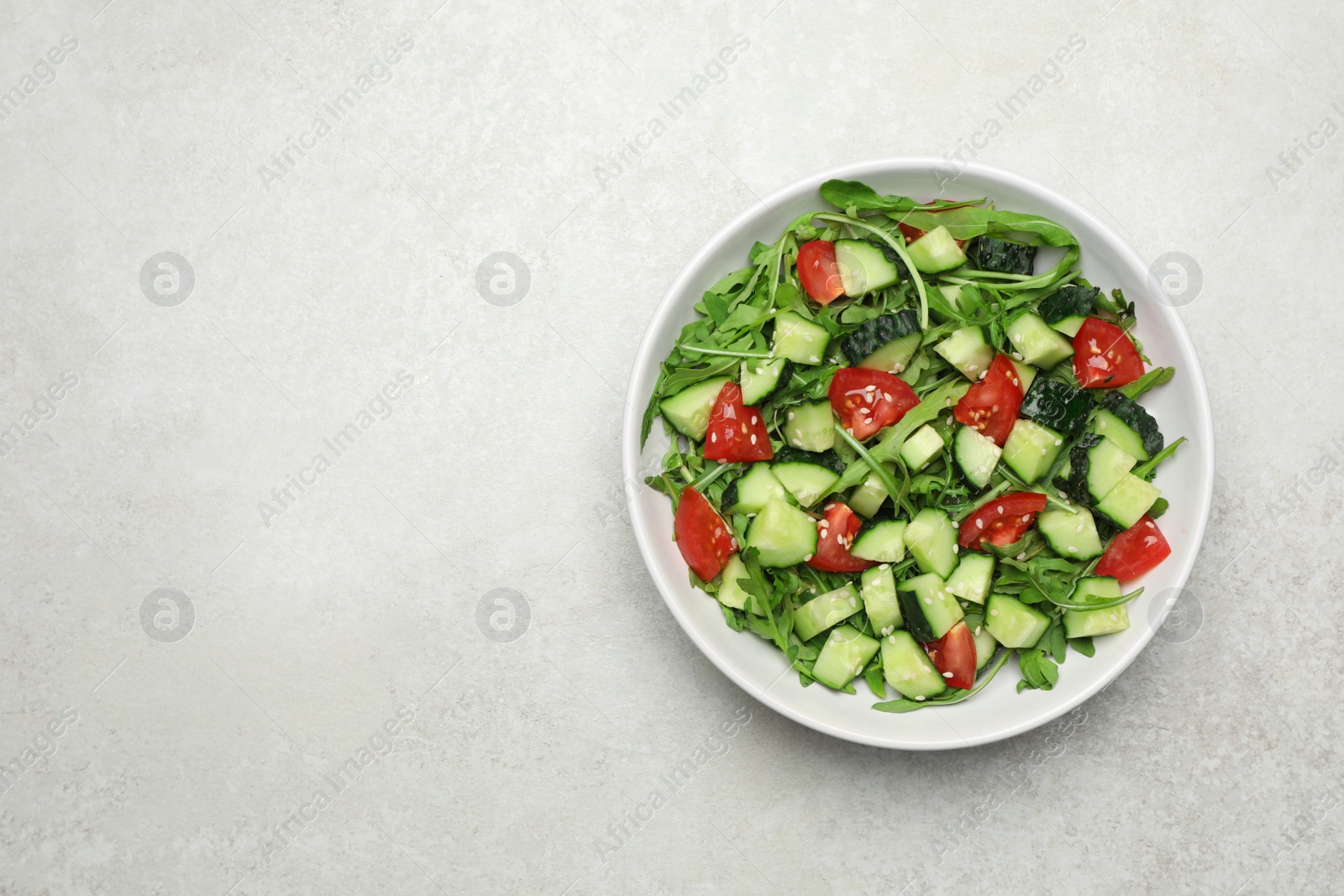 Photo of Delicious salad with cucumbers, tomatoes and sesame in bowl on light table, top view. Space for text