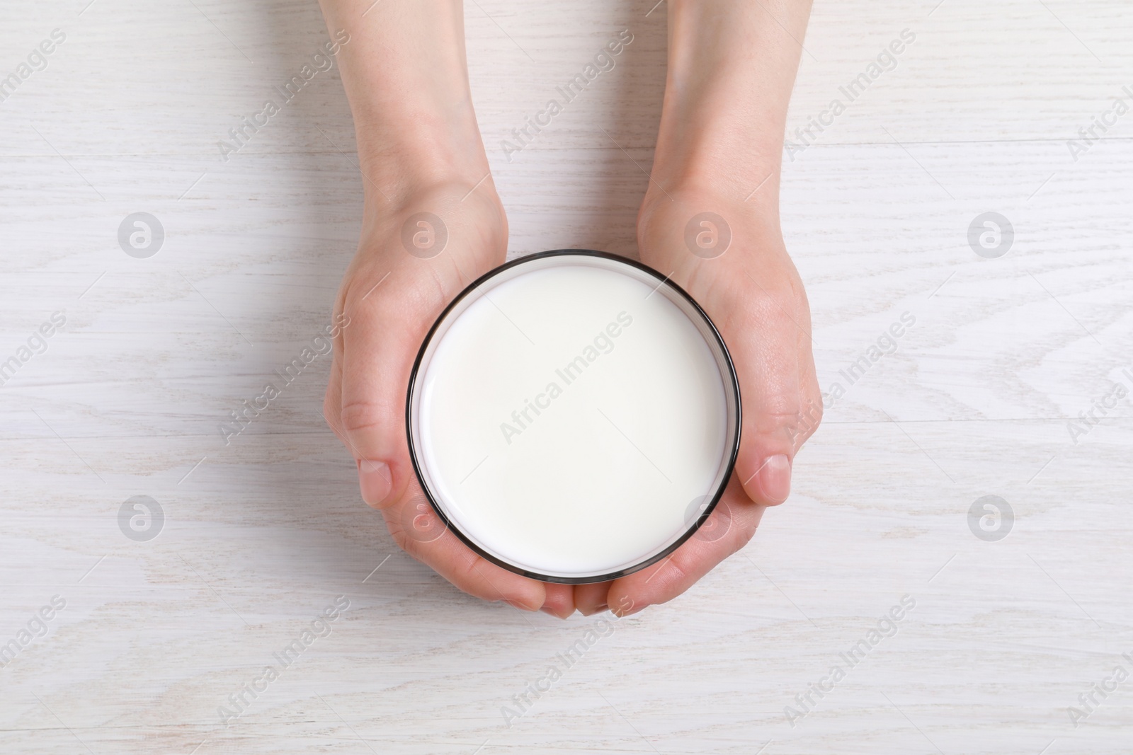 Photo of Woman holding glass of milk at white wooden table, top view