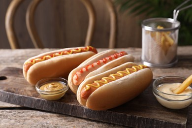 Delicious hot dogs with sauces and French fry on wooden table, closeup