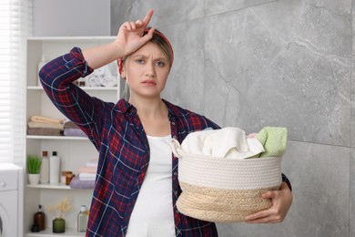 Photo of Tired woman with basket full of laundry in bathroom