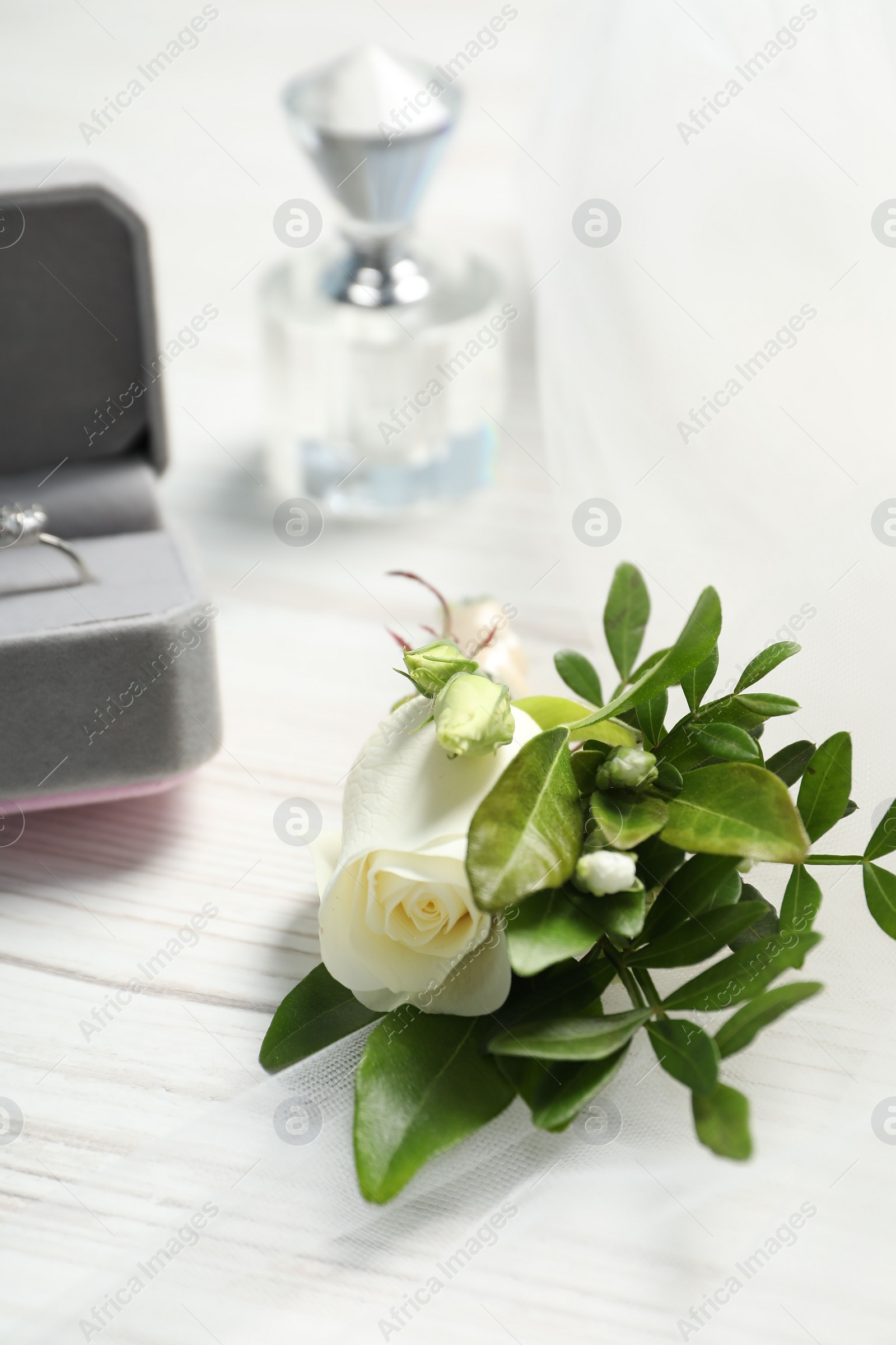 Photo of Wedding stuff. Stylish boutonniere, perfume and ring on white wooden table, closeup