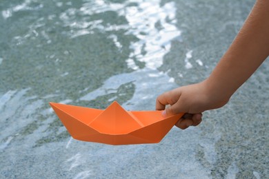 Photo of Kid launching small orange paper boat on water outdoors, closeup