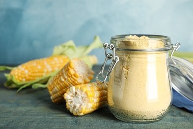 Photo of Corn flour in glass jar and fresh cobs on blue wooden table