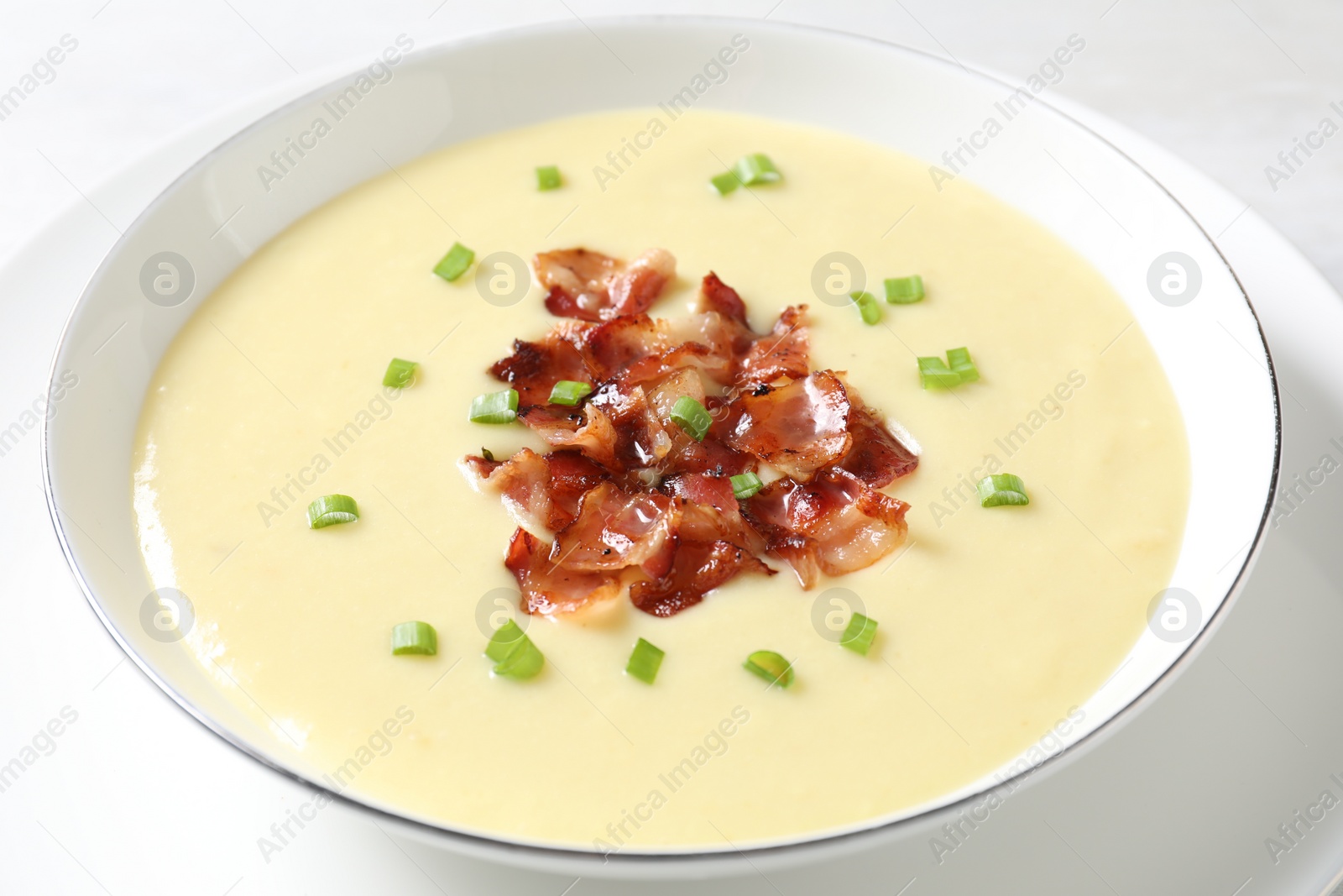 Photo of Tasty potato soup with bacon and green onion in bowl on white table, closeup