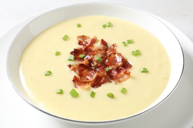 Tasty potato soup with bacon and green onion in bowl on white table, closeup