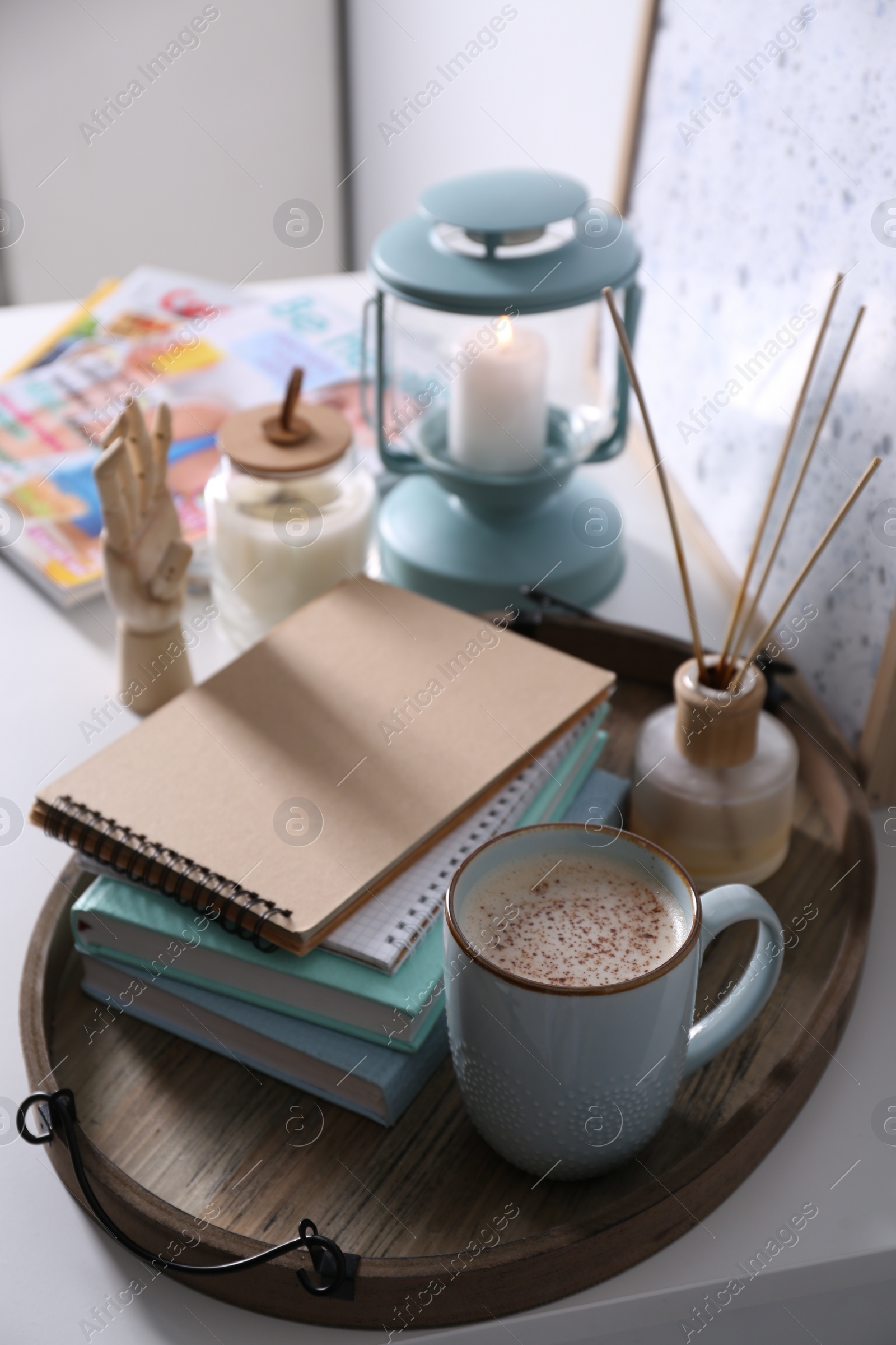 Photo of Wooden tray with books, air reed freshener and cup of coffee on white table indoors