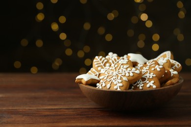 Tasty Christmas cookies with icing in bowl on wooden table against blurred lights. Space for text