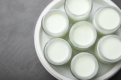 Photo of Modern yogurt maker with full jars on dark grey table, top view. Space for text