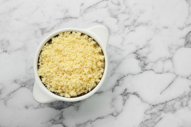 Photo of Bowl of tasty couscous on white marble table, top view. Space for text