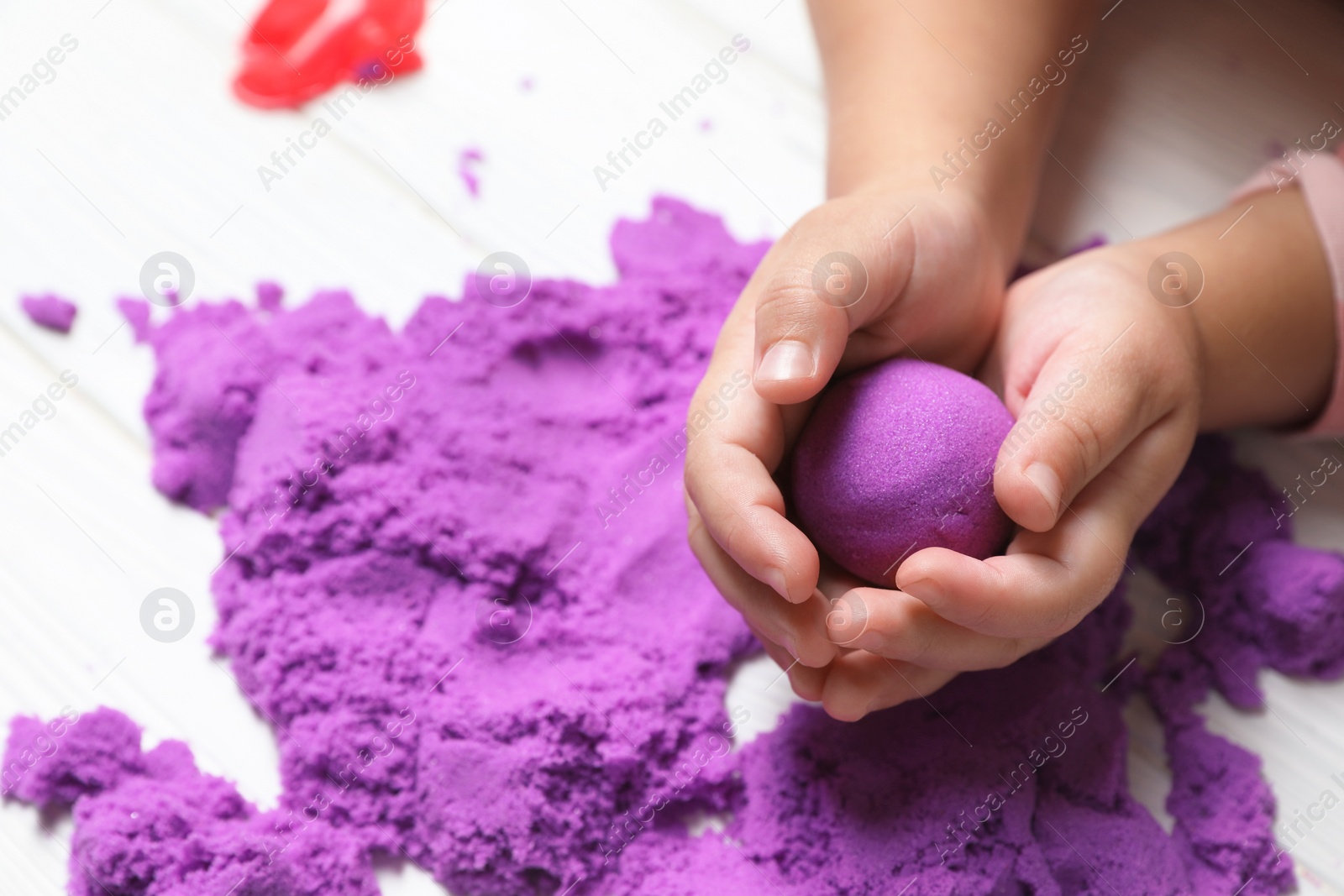 Photo of Little child playing with kinetic sand at white table, closeup