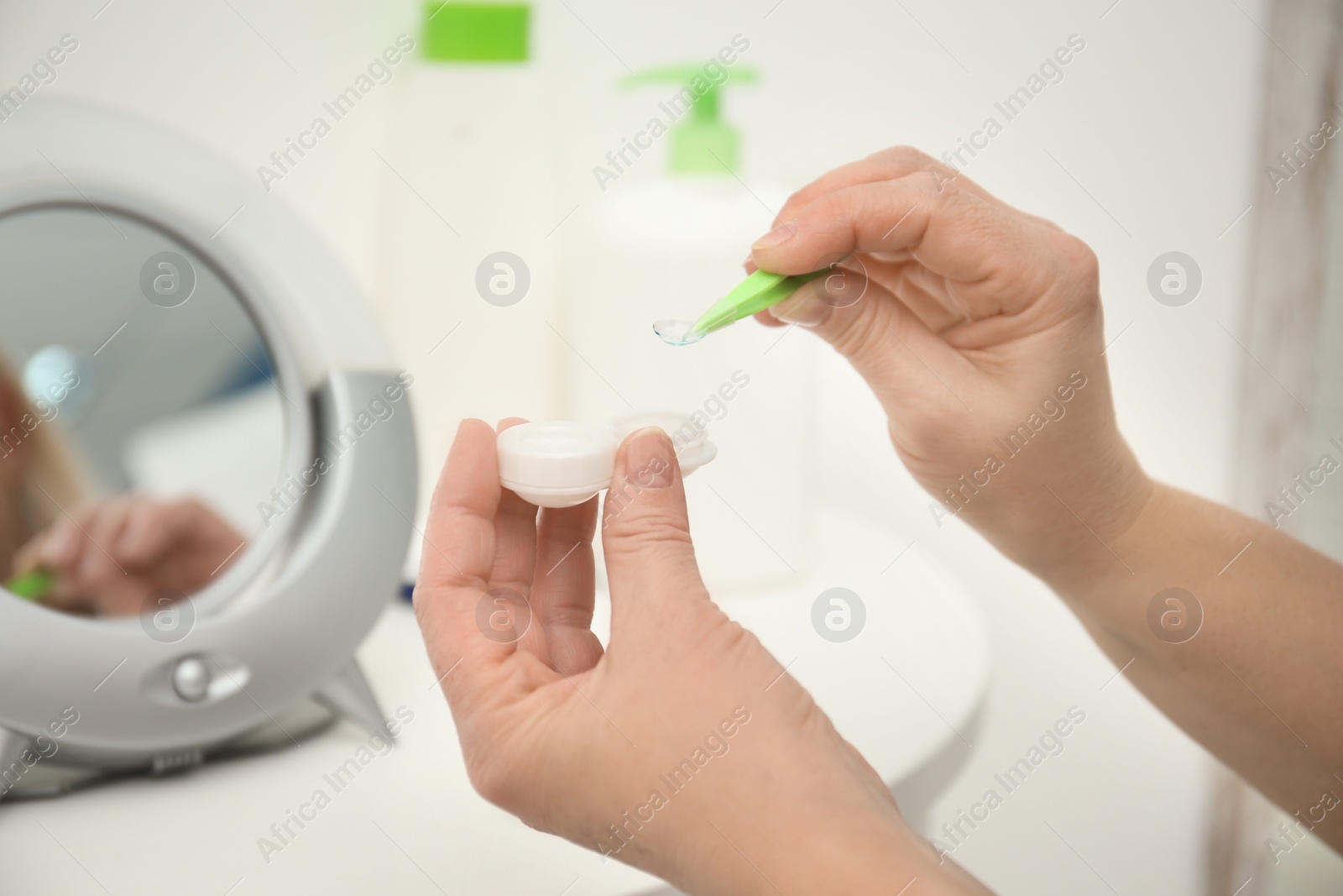 Photo of Senior woman taking contact lens from container in front of mirror