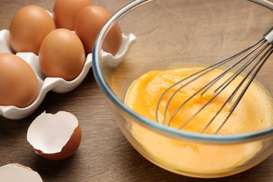 Photo of Whisking eggs in glass bowl on wooden table, closeup