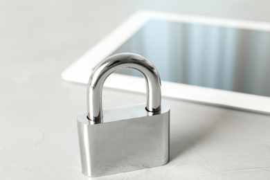 Photo of Metal lock and tablet on light grey table, closeup. Protection from cyber attack