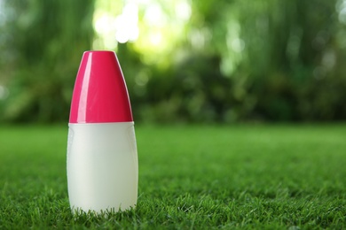 Photo of Bottle of insect repellent spray on green grass. Space for text