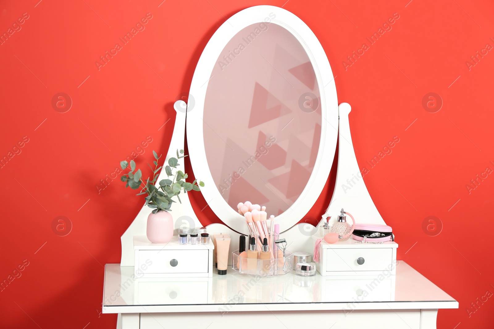 Photo of Dressing table with mirror and makeup products near red wall