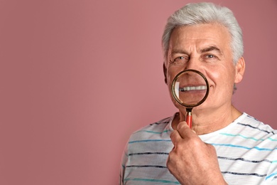 Photo of Mature man with healthy teeth and magnifier on color background. Space for text