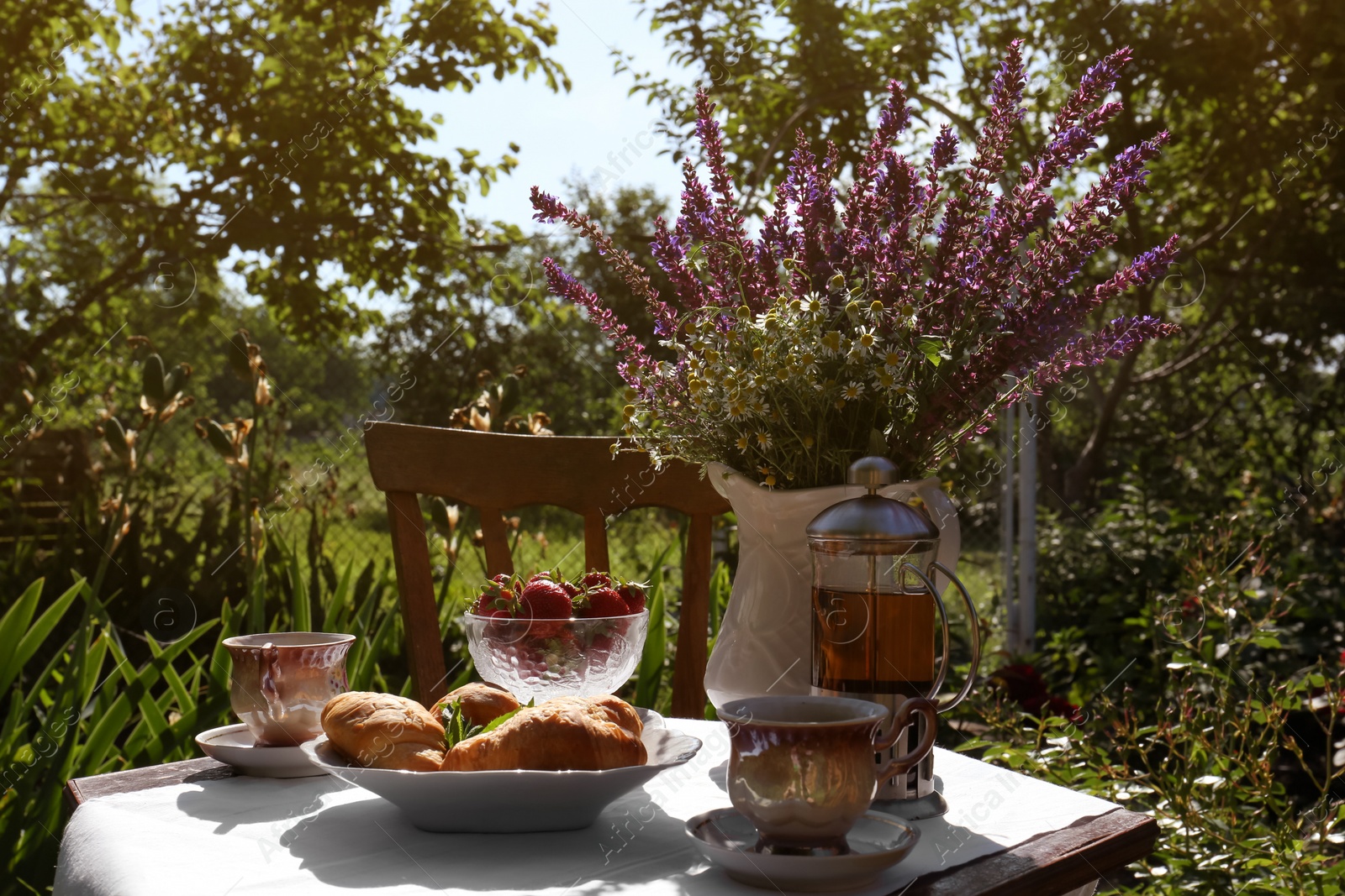 Photo of Beautiful bouquet of wildflowers on table served for tea drinking in garden