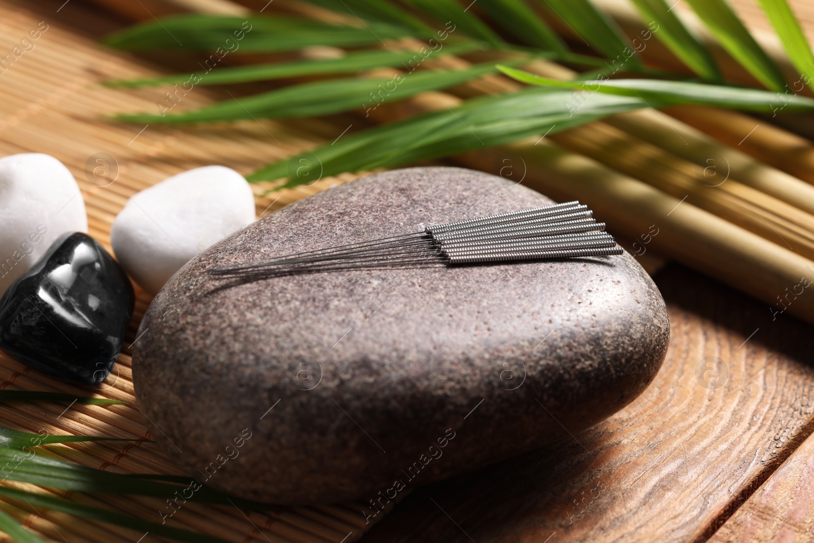 Photo of Stone with acupuncture needles on wooden table