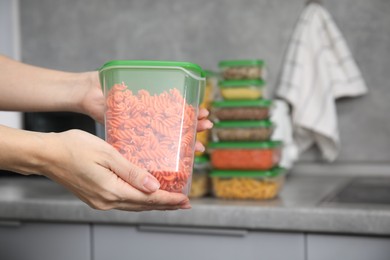 Photo of Woman with plastic container of raw pasta in kitchen, closeup and space for text. Food storage