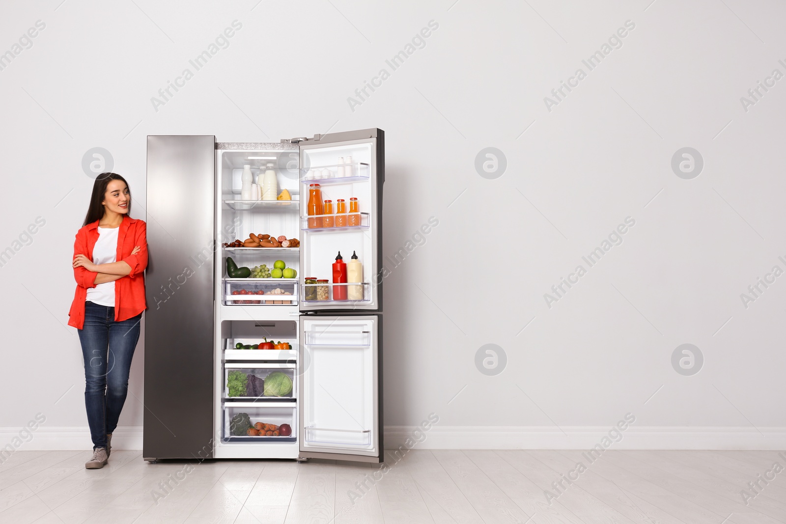 Photo of Happy young woman near open refrigerator indoors, space for text