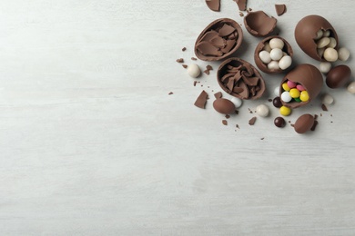 Photo of Broken chocolate eggs with candies on white wooden table, flat lay. Space for text