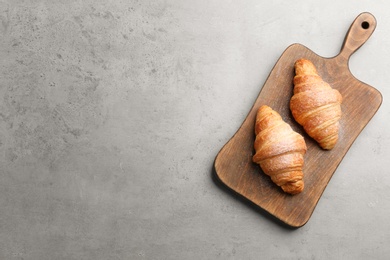 Photo of Wooden board with tasty croissants and space for text on grey background, top view. French pastry
