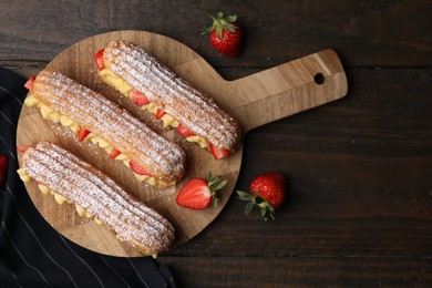 Photo of Delicious eclairs filled with cream and strawberries on wooden table, top view. Space for text