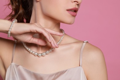 Photo of Young woman wearing elegant pearl jewelry on pink background, closeup