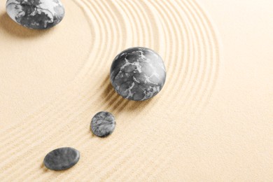 Photo of Zen garden stones on beige sand with pattern, flat lay