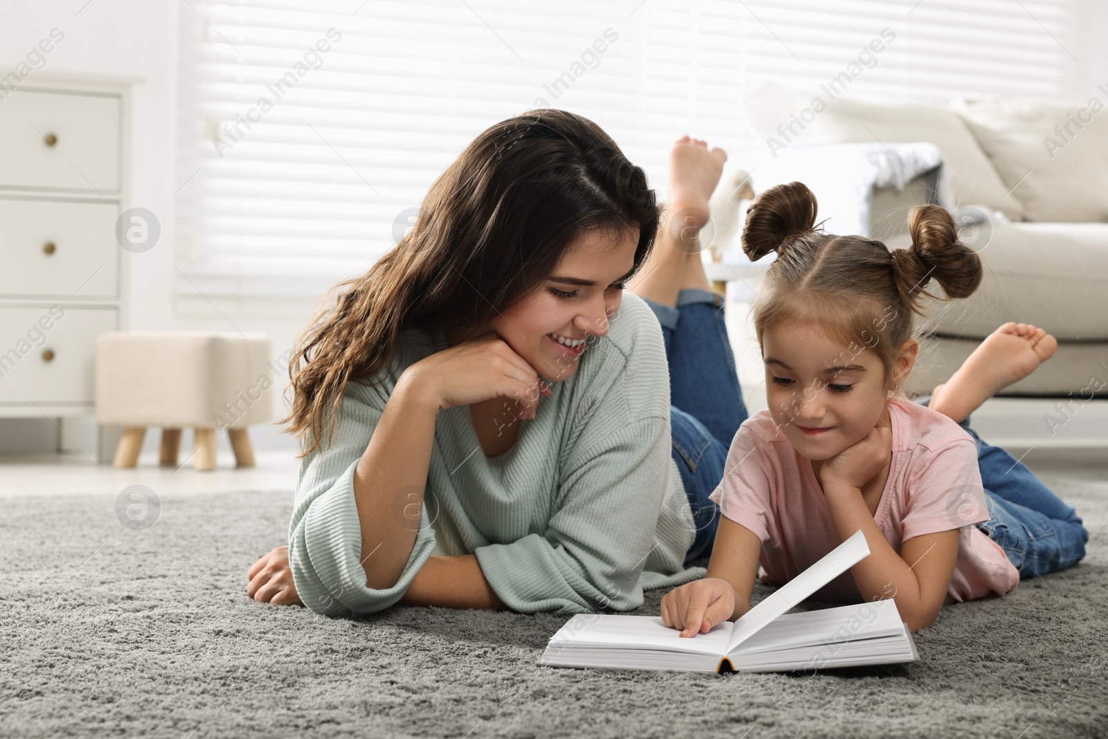 Photo of Young mother and her daughter reading book on floor at home